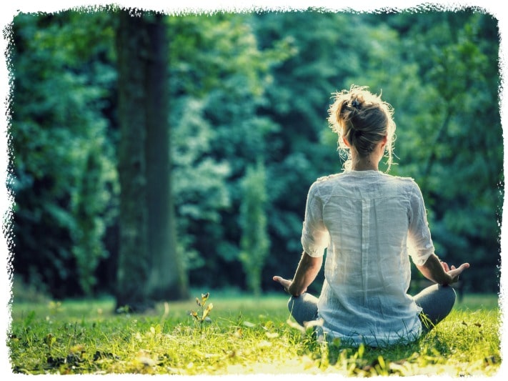 A woman meditating while sitting on a grass field how to love yourself.
